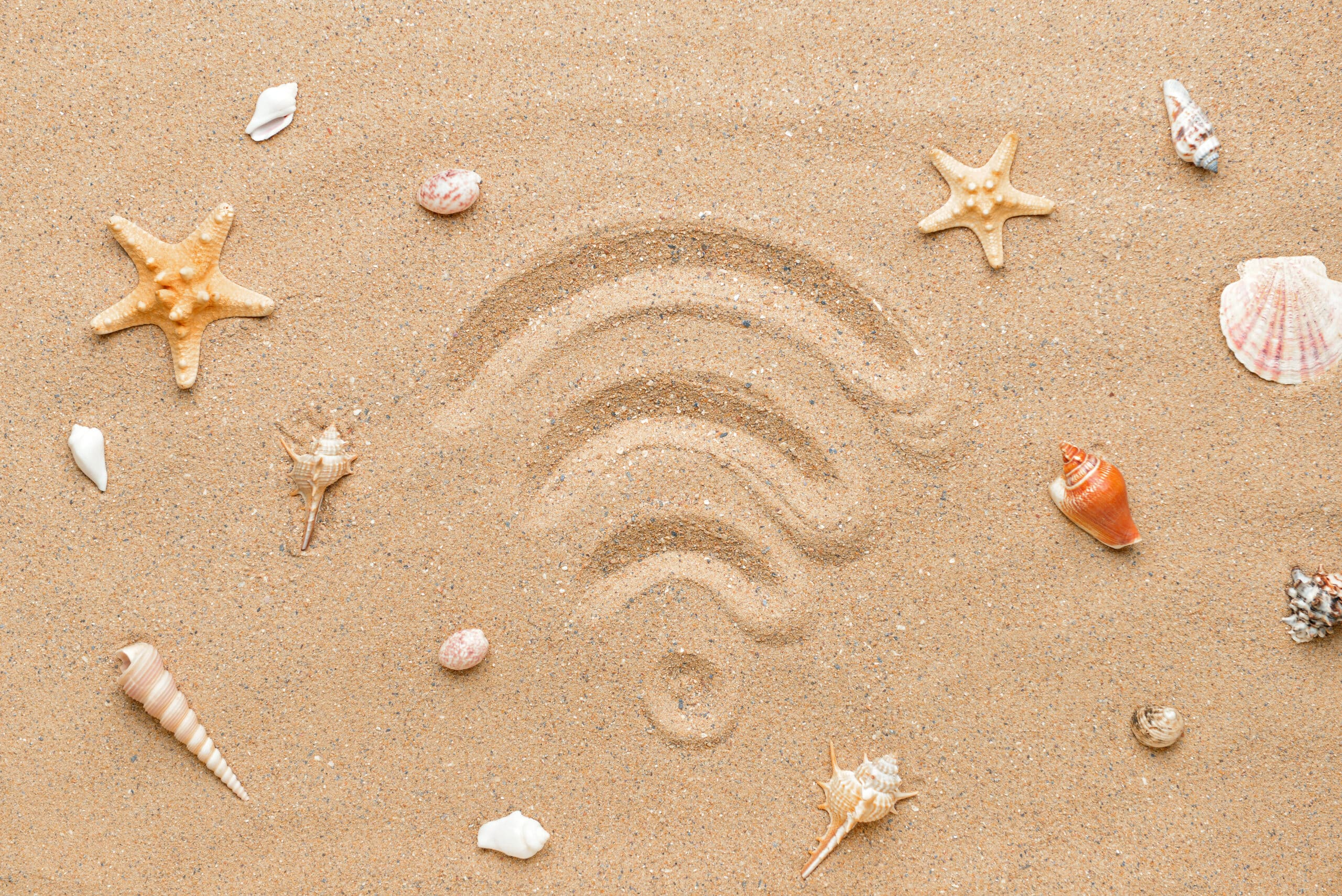 Wi-Fi symbol drawn in beach sand, surrounded by seashells and starfish